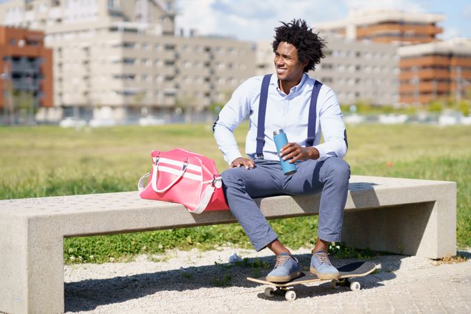 Man in suspenders on concrete bench with skateboard