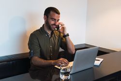 Cheerful man talking on smartphone near laptop