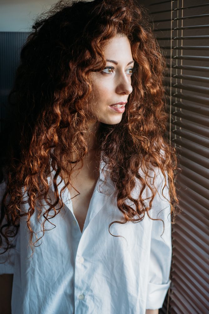 Beautiful thoughtful woman standing by a windows blind