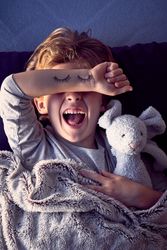 Irritated boy covering eyes and creaming in bed