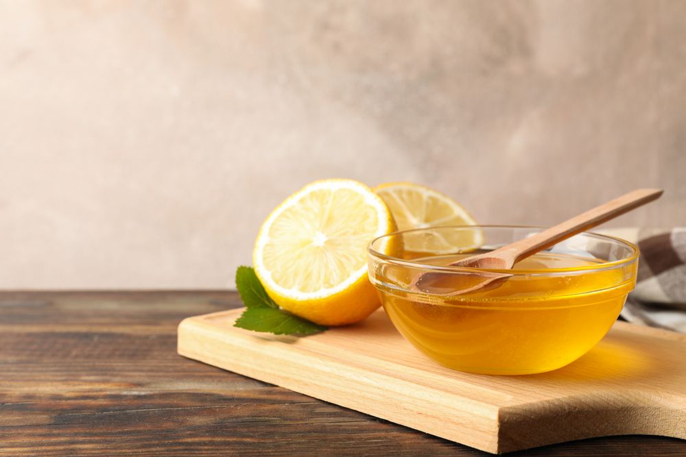 Lemons and bowl with honey and dipper on wooden background, space for text