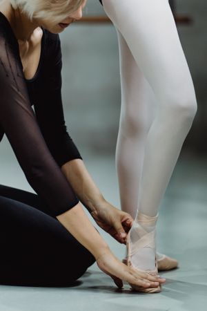 Cropped image of ballet instructor fixing dancer's shoes