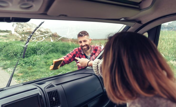 Woman sitting inside van as her boyfriend cleaners front windshield on overcast day