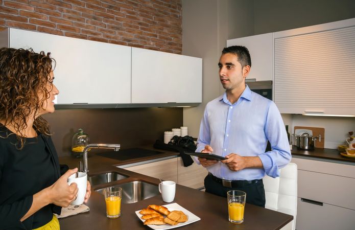 Man holding tablet while talking with curly haired woman at breakfast in home