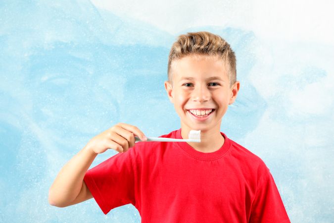 Boy with toothbrush on color background, space for text
