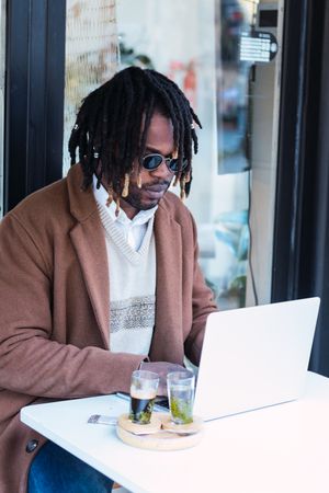 Black man browsing on laptop on restaurant terrace