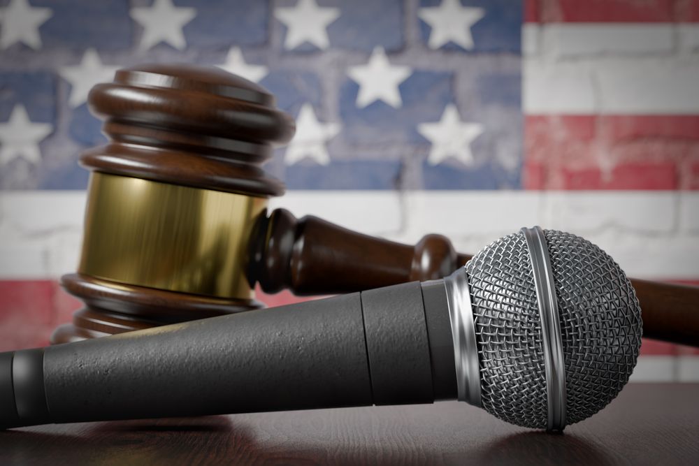 Microphone and Gavel Resting on a Table with the American Flag Painted On A Brick Wall Behind.