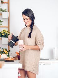 Positive female pouring hot coffee from moka pot in kitchen