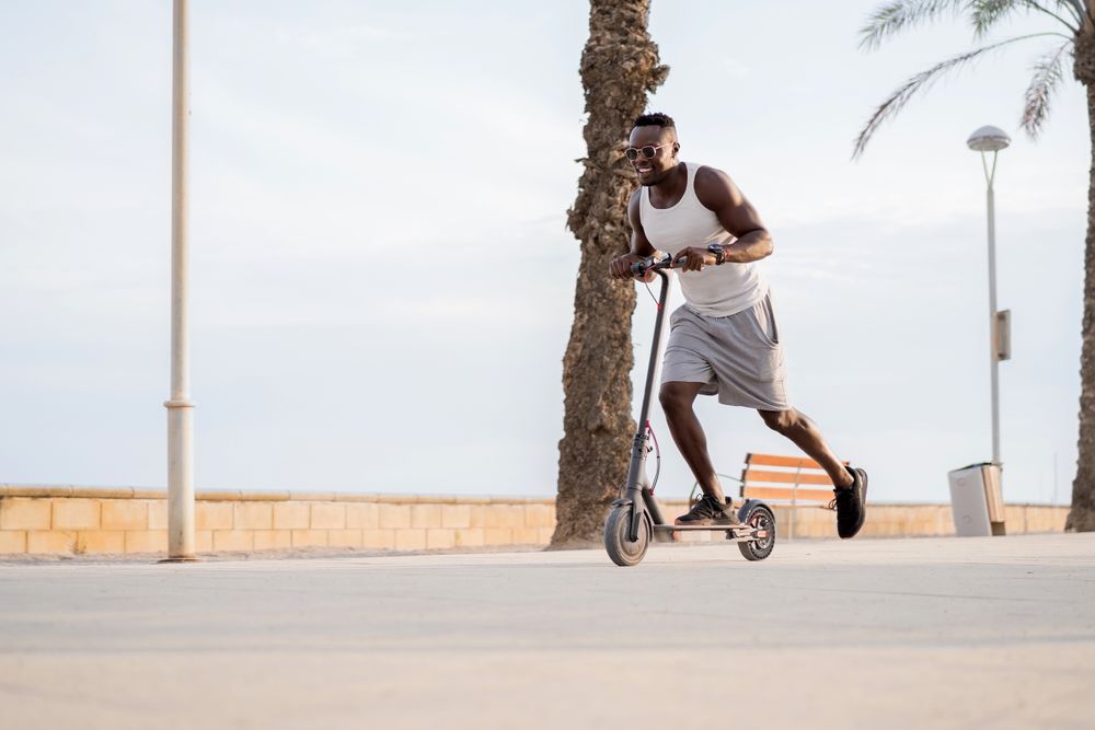 Cool adult Black man riding scooter in street