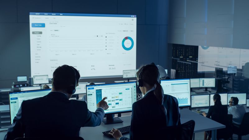 Data Analysts Collaborate in Dimly Lit Office, Examining Multiple Screens Displaying Charts and Graphs.