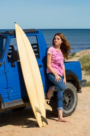 Woman with surfboard near car at seaside