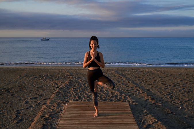 Content Hispanic woman practicing Vrikshasana posture near sea