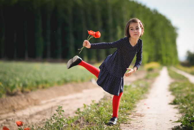 Girl on one leg posing for photo with red flowers in her hand