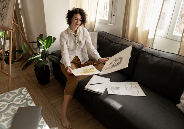 Woman drawing on papers on sofa in room