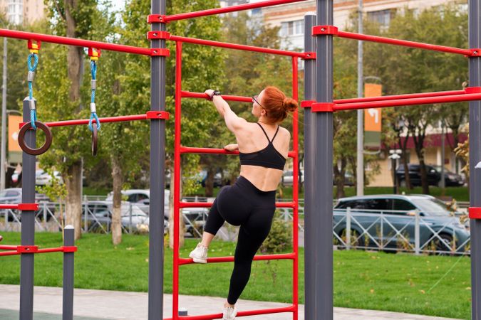 Woman climbing red outdoor fitness structure in park.