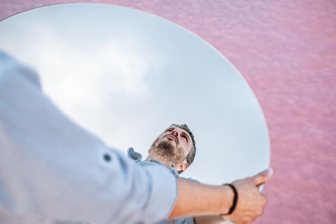 Stylish man holding mirror with reflection