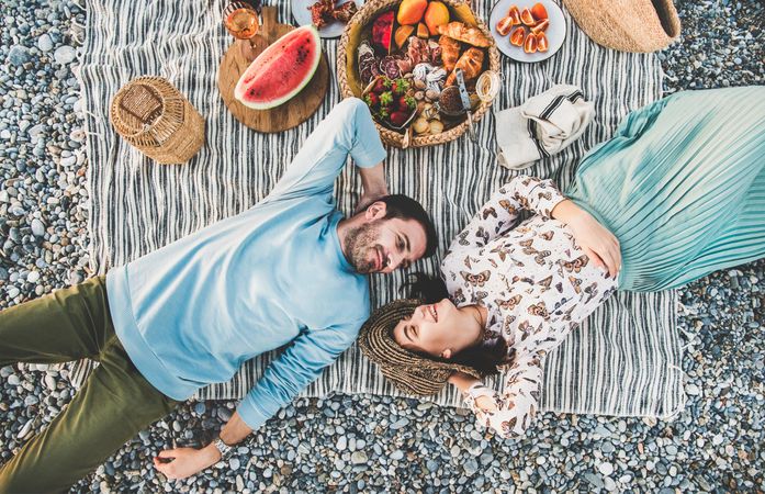 Couple lying next to picnic with watermelon, breads, oranges, and wine