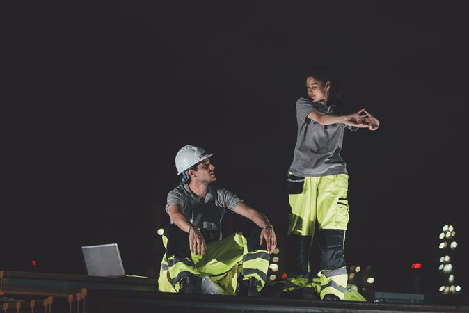 Female worker stretching body, Male colleagues sit for taking a break, relax, resting after work, construction site at night, overtime working late