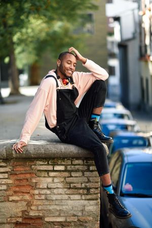 Calm male sitting with one leg up on brick wall in city