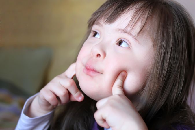 Portrait of a girl with Down syndrome with her fingers on her cheeks