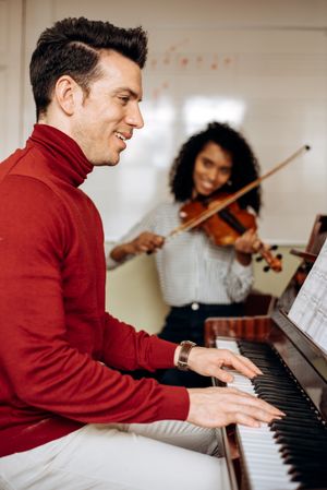 Man playing piano near woman playing violin in studio