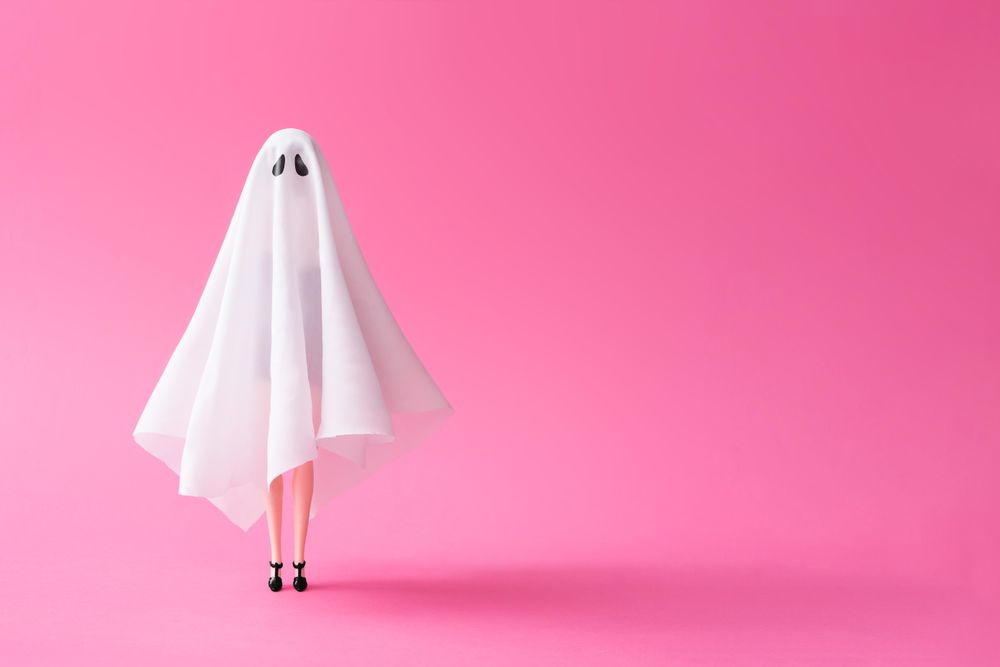 Doll under ghost sheet costume against pastel pink background