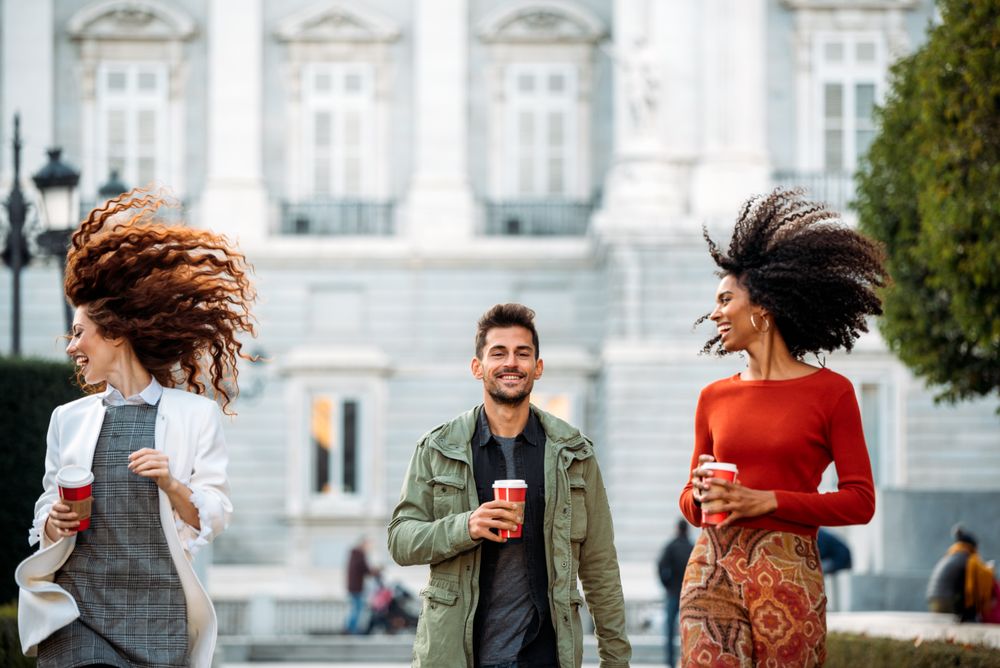 Three young friends walking and drinking coffee
