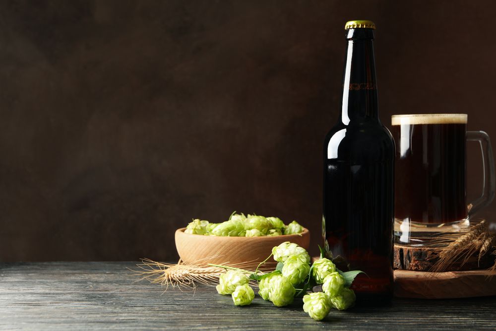 Beer, hop and wheat on wooden table against brown background