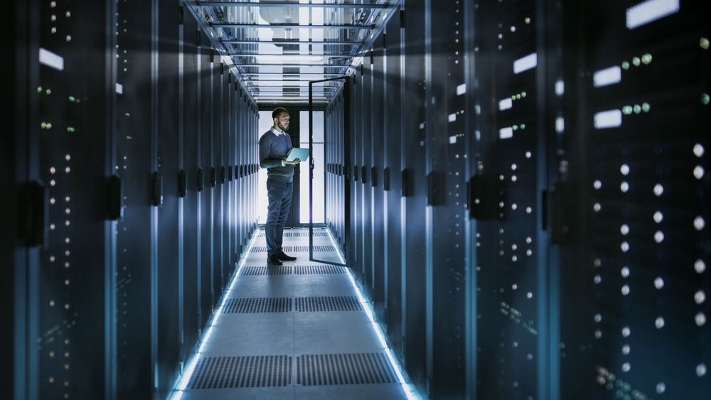IT Technician Works on Laptop in Big Data Center full of Rack Servers.