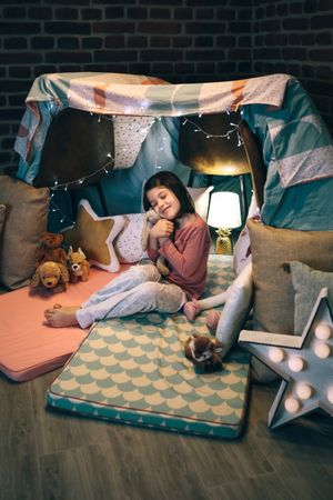 Girl hugging stuffed doll playing in a diy tent at home