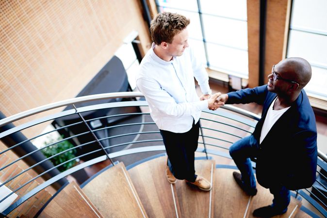 Two colleagues shaking hands on a spiral staircase