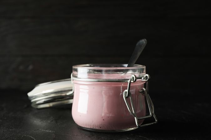 Glass jar with fruit yogurt on dark cement background, space for text