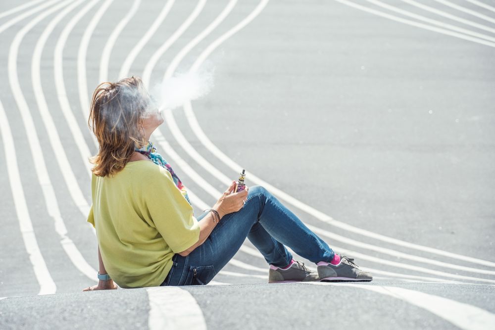 Modern relaxed woman vaping while sitting on marked road