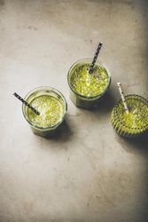 Three green smoothies in glasses with eco friendly straws on concrete background, copy space
