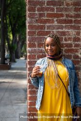 Portrait of woman with box braids standing in front of brick wall smiling and looking at camera 432Lr5