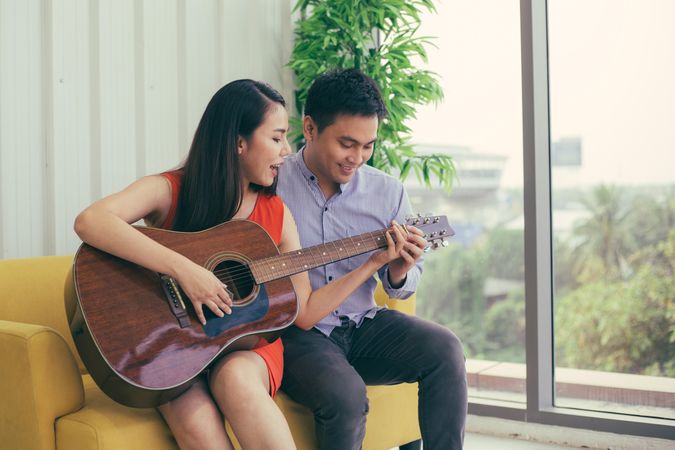 Man and woman having fun playing guitar on yellow couch