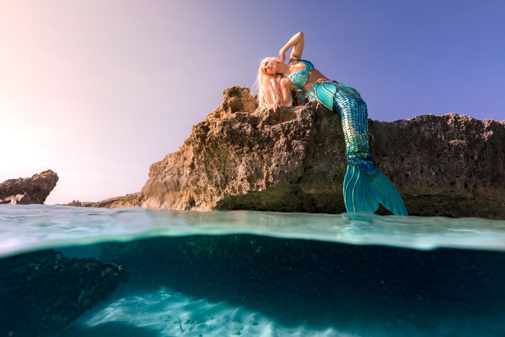 Blond fairytale female mermaid lying on rock