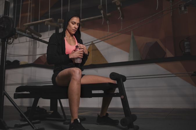 Athletic woman looking at watch on bench at gym