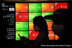 Two people with facemasks standing beside Indonesian stock market screen 0PJZO4