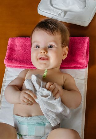 Cute baby playing with towel during diaper change, vertical