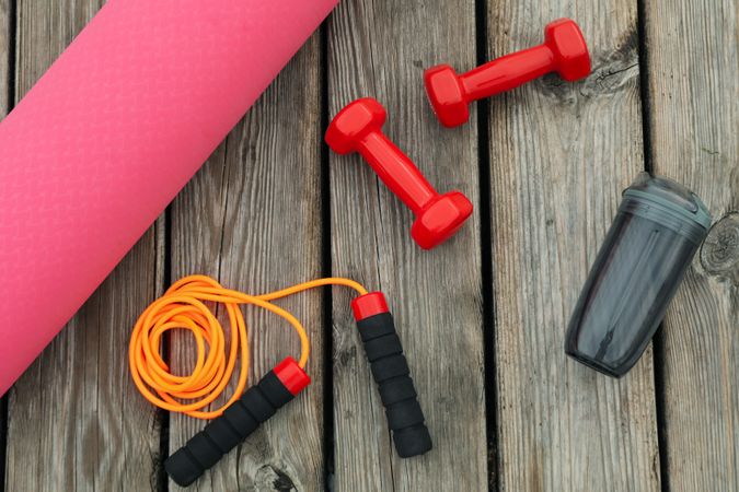 Yoga mat, water bottle, jump rope and dumbbells on wooden background, top view