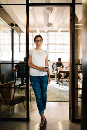 Young woman at office doorway holding a coffee