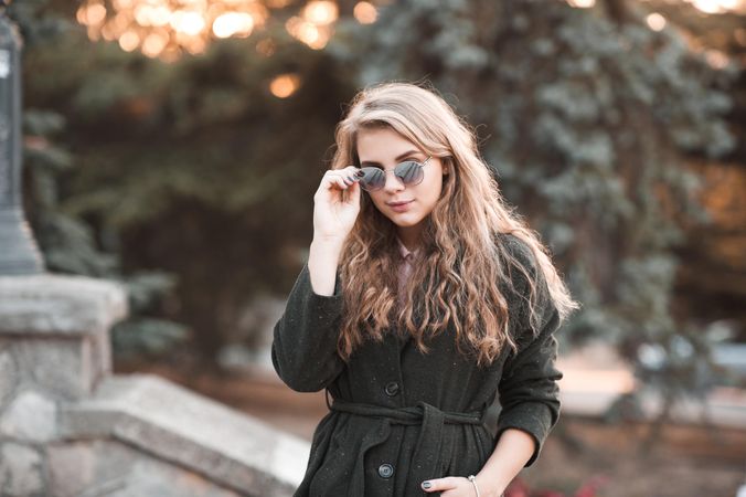 Teenage girl in dark coat wearing sunglasses and posing outdoor
