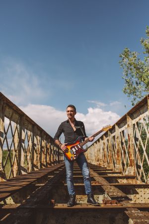 Man with guitar standing on bridge