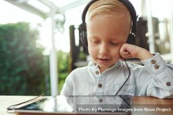 Blond boy using headphones and watching show or playing game on digital tablet 5l8Am5