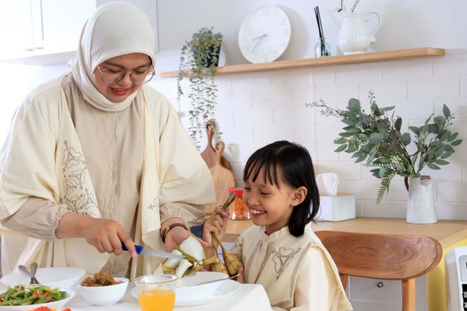 Muslim Woman Serving Ketupat, Cutting to Small Piece to Her Kids in Dining Room While Having Dinner During Eid Mubarak