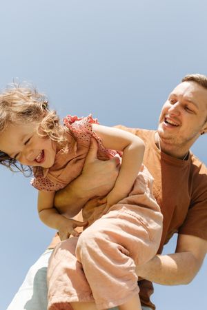 Happy father holding playful daughter against cloudless sky