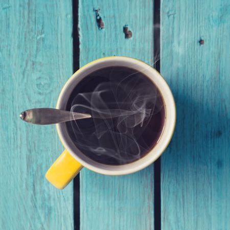 Hot fresh coffee with steam rising on blue wooden background