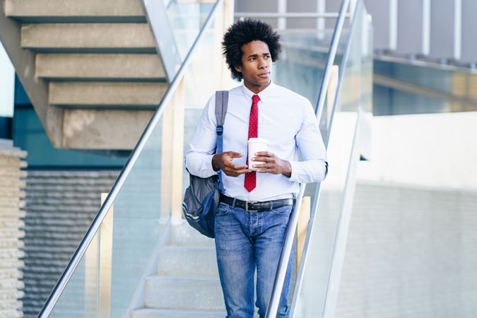 Calm man holding coffee walking down stairs