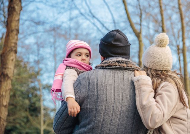 Father holding up young daughter as they stand looking at fall